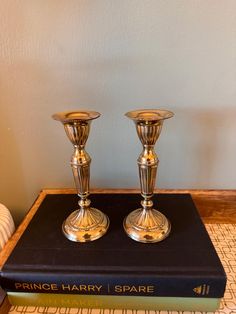 two golden candlesticks sitting on top of a book next to a lamp shade