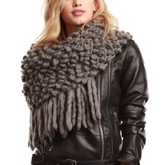 a woman wearing a black leather jacket and gray knitted scarf with fringes on it