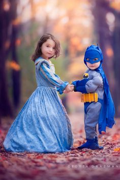 two children dressed up as batman and princesses in the woods with leaves on the ground