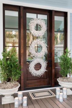 the front door is decorated with wreaths, candles and potted plants on the porch