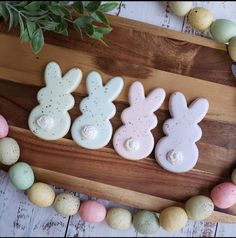 three decorated cookies sitting on top of a wooden cutting board next to eggs and flowers