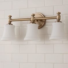 three light bathroom fixture with white shades on the wall and brick tiles in the background