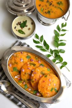 some food is sitting on a table next to silver bowls and spoons with green leaves