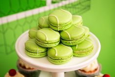 a white cake plate topped with green macaroons and cupcakes covered in frosting