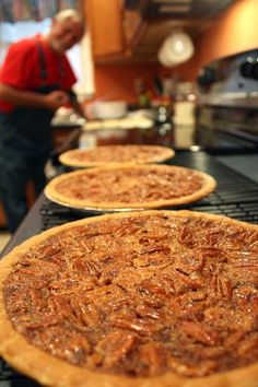 three pizzas sitting on top of an oven in front of a man preparing food