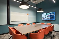 an office meeting room with orange chairs and a flat screen tv mounted on the wall