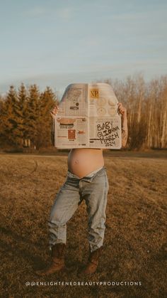 a pregnant woman holding up a newspaper over her head while standing in an open field