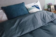 a bed with blue sheets and pillows on top of it next to a night stand