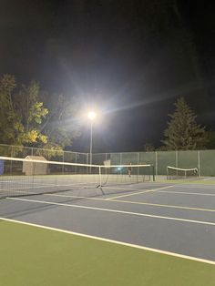 two people playing tennis at night on an outdoor court with lights in the dark behind them