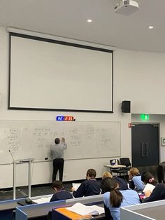 people are sitting at desks in front of a whiteboard with writing on it