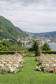 an outdoor ceremony set up with white chairs and flowers on the grass, overlooking a lake