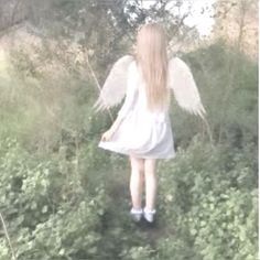 a girl with white wings is walking through the grass and bushes in front of her