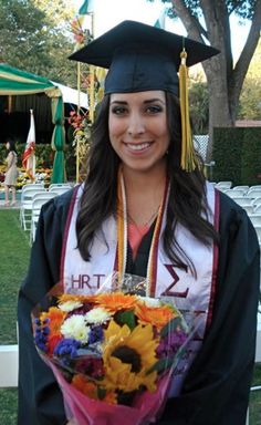 a woman wearing a graduation cap and gown holding a bouquet of flowers in her hands