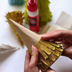 a person is holding a paper cone with gold foil on it and some other crafting supplies in the background