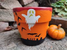 a painted pot sitting on top of a rock next to some pumpkins and plants