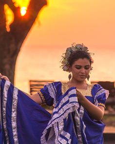 a woman in blue and white dress holding up a piece of cloth with the sun setting behind her