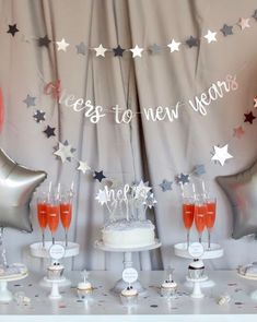 a table topped with cake and drinks next to silver foil balloons that say happy new year