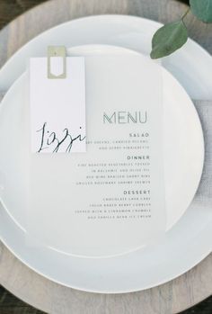 a white plate topped with a menu next to a green leafy plant on top of a wooden table