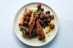 a white plate topped with meat covered in olives and sauce on top of a table