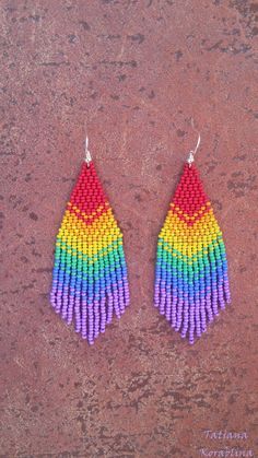 a pair of earrings with multicolored beads hanging from the side on a brown surface