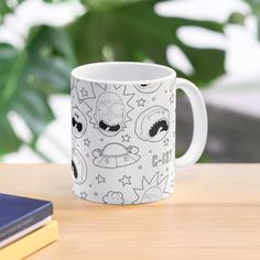 a white coffee mug sitting on top of a wooden table next to a book and plant