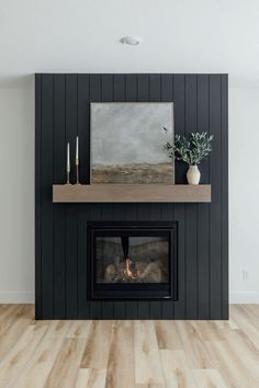 a fireplace with black paneling and a painting on the mantel above it in a living room