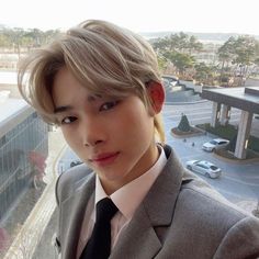 a young man wearing a suit and tie standing in front of a window looking at the camera