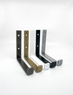 four different colored metal brackets on a white background with one black, the other gold and silver