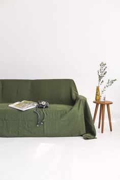 a couch covered in a green cover next to a table with a vase on it