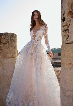 a woman in a white wedding dress standing by some stone pillars with her hands on her hips