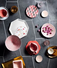 several plates and cups on a tiled floor with flowers in the middle one is empty