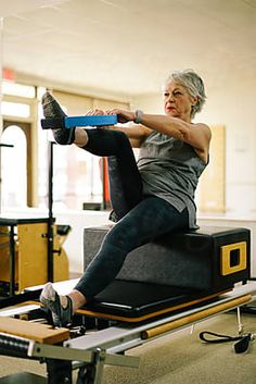 an older woman is doing exercises on a rowing machine in a room with other equipment