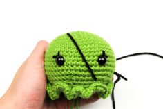 a hand holding a green crocheted object with black eyes and an eyeball attached to it