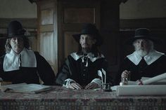 three people sitting at a table with books in front of them and one person wearing a top hat