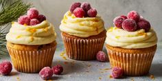 three cupcakes with frosting and raspberries on top, surrounded by pine branches