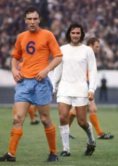 two men in orange and blue soccer uniforms are standing near each other on the field