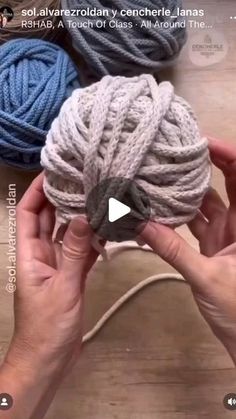 two hands holding balls of yarn on top of a wooden table