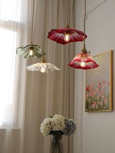 three lights hanging from the ceiling above a vase with flowers in front of a window