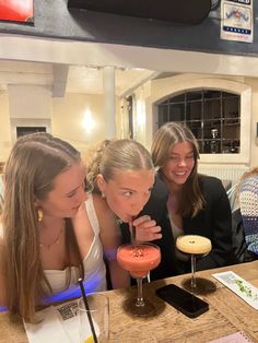 three women sitting at a table with drinks in front of them and one woman standing behind the bar