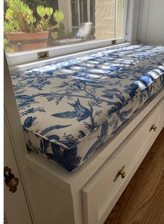 a blue and white bed sitting on top of a wooden dresser next to a window