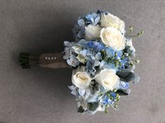 a bridal bouquet with white roses and blue hydrangeas is seen from above