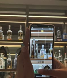 a person holding up a cell phone to take a photo in front of liquor bottles