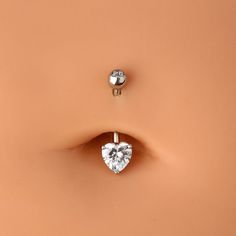 a pair of heart shaped diamond earrings on top of a tan surface with the earring in the shape of a heart