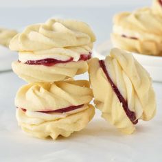 three cookies with white frosting and raspberry fillings on top are stacked next to each other