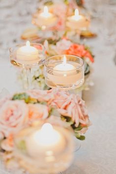 some candles are sitting on a table with pink flowers and greenery around the edges