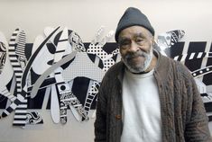 an older man standing in front of a wall with black and white artwork on it