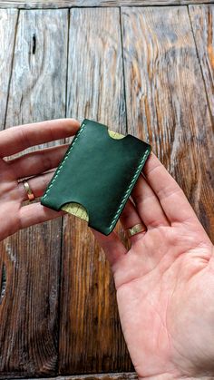 a hand holding a green leather wallet on top of a wooden table next to a piece of wood