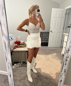 a woman taking a selfie in front of a mirror wearing a white fringe skirt and cowboy boots