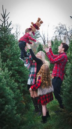 a man and woman are playing with their child in the christmas tree farm while they both wear plaid outfits