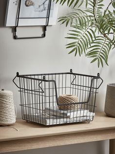 a wire basket sitting on top of a wooden table next to a potted plant